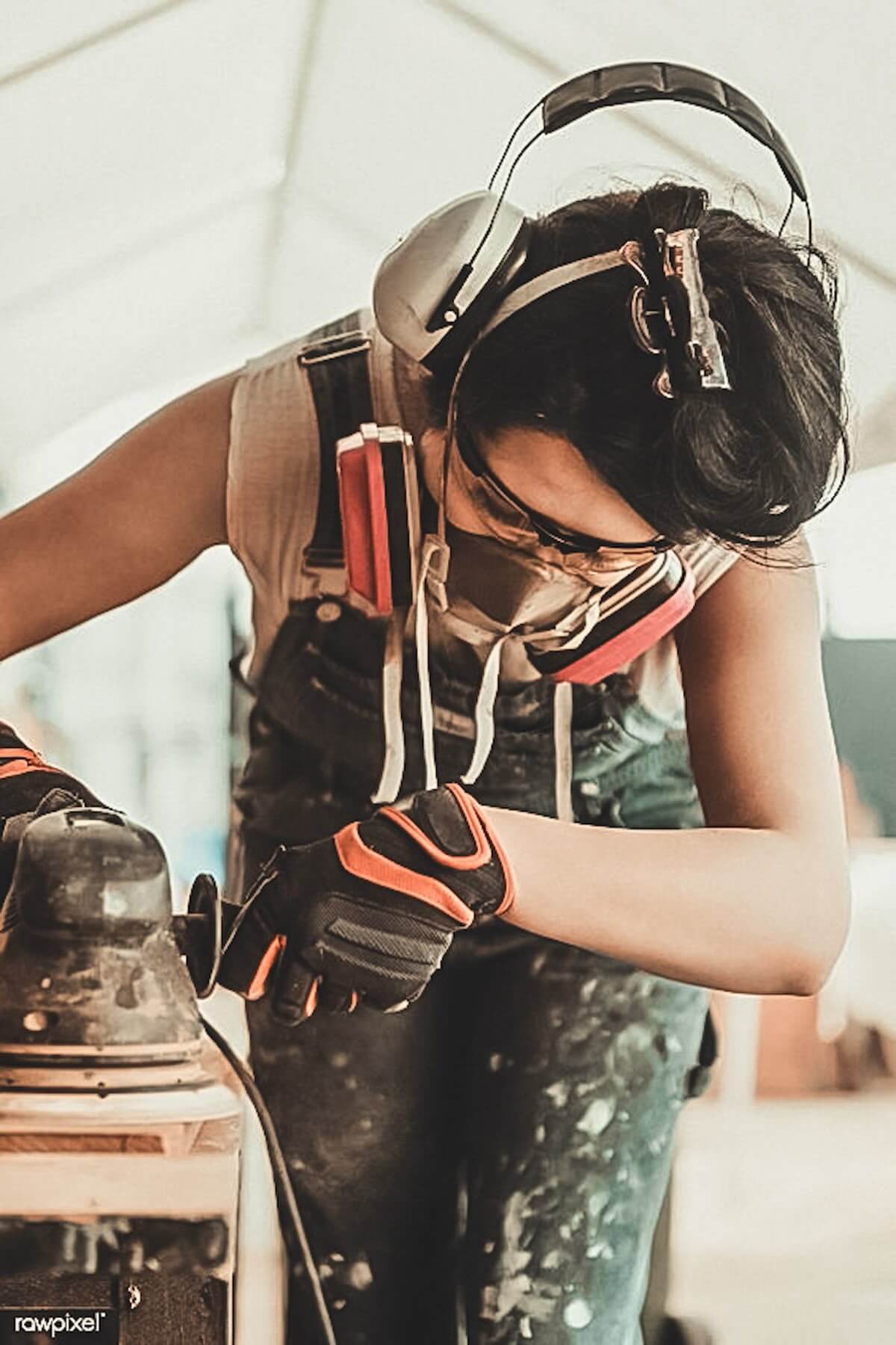 Tradesperson wearing safety gear sanding wood with a power tool.